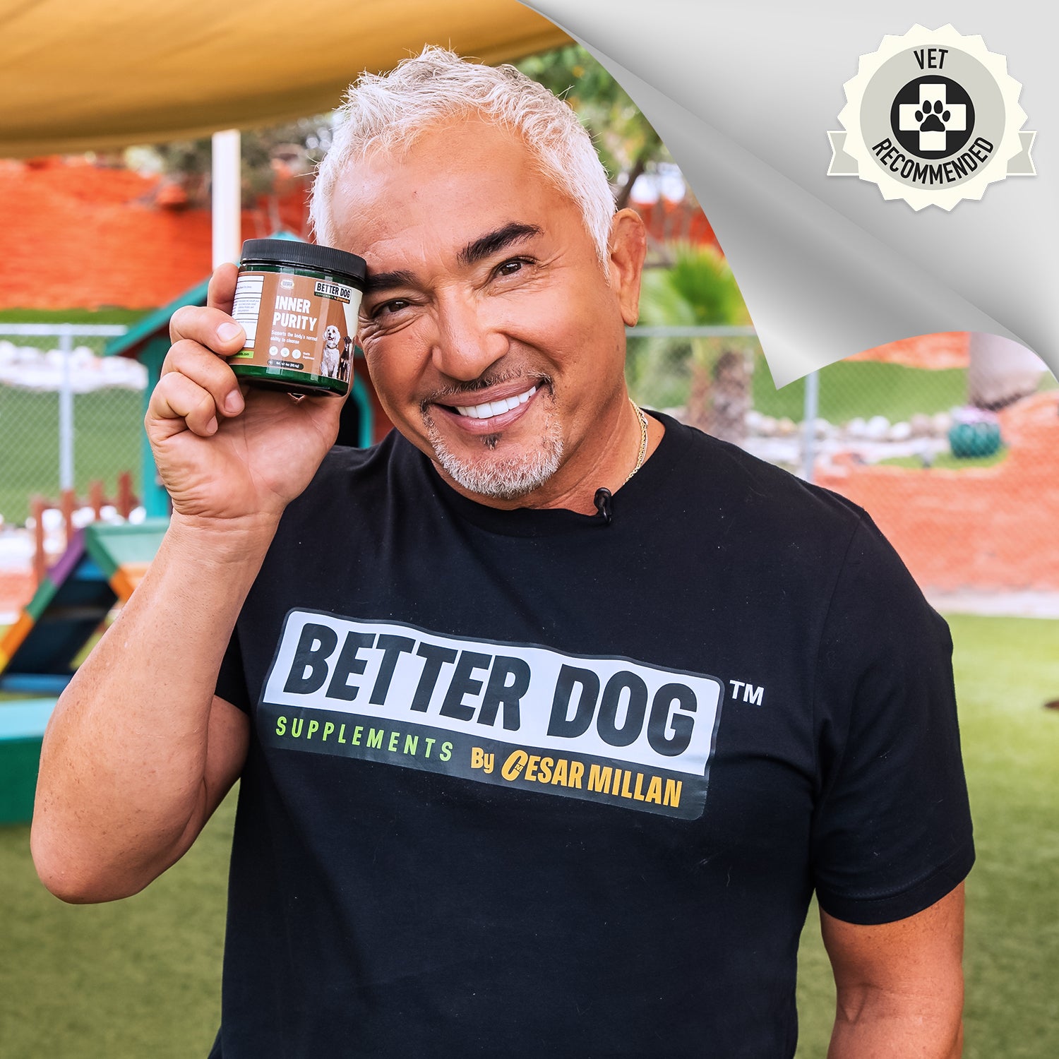 Cesar Millan smiling and holding a jar of Better Dog “Inner Purity” supplement in an outdoor park setting, with a “Vet Recommended” badge in the corner.